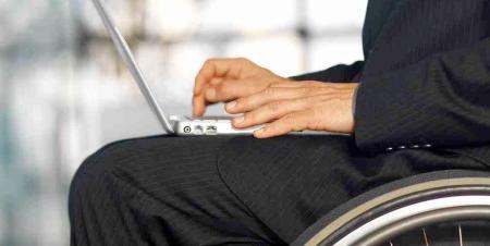 一个男人穿着西装，坐在轮椅上，使用笔记本电脑.